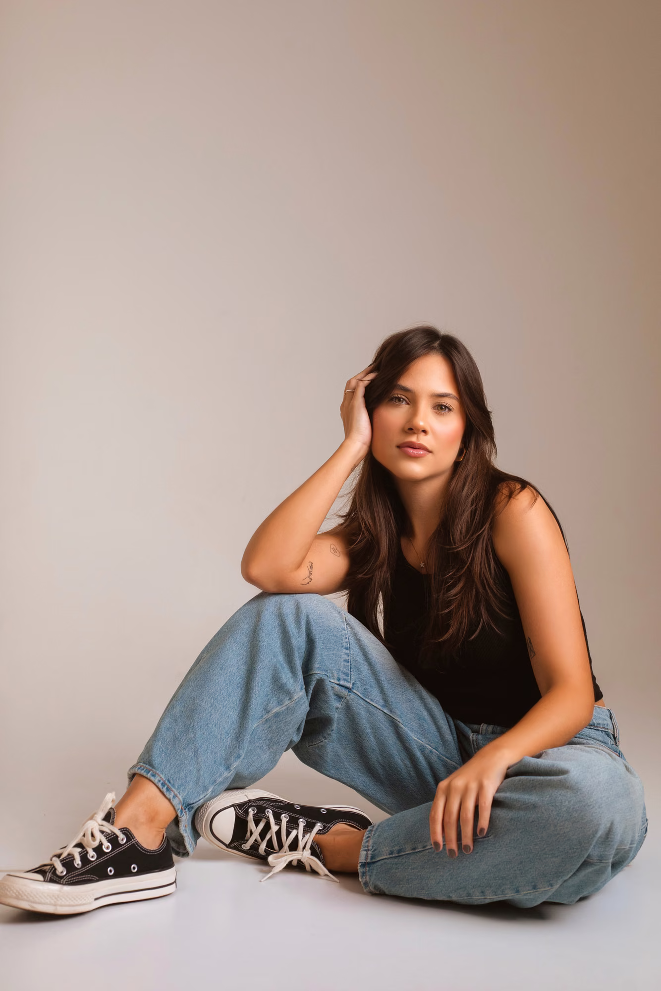 Clara Diniz sentada no chão, de calça jeans e regata preta